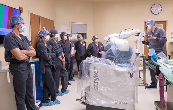 NIHD Orthopedic surgeon Dr. Richard Meredick (left) and the NIH Surgery Team listen as Stryker’s Mako Instructor Javen Spire (far right) walks the team through a mock Mako SmartRobotics-assisted total knee replacement. The surgery team, from left are Danielle Medeiros, Oscar Morales (standing behind Medeiros), Cheryl Carter, Toni Rhodes, Chris Cauldwell, Lisa Wray and Nita Eddy. 
